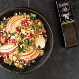 Salad with apples and pomegranate seeds next to a bottle of Olivelle Harvest Fig balsamic on a dark surface
