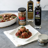 Plated dish of meatballs with red sauce, surrounded by Olvelle products on a gray surface.