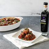 Bowl of meatballs with a bottle of Olivelle dark balsamic vinegar on a gray surface.
