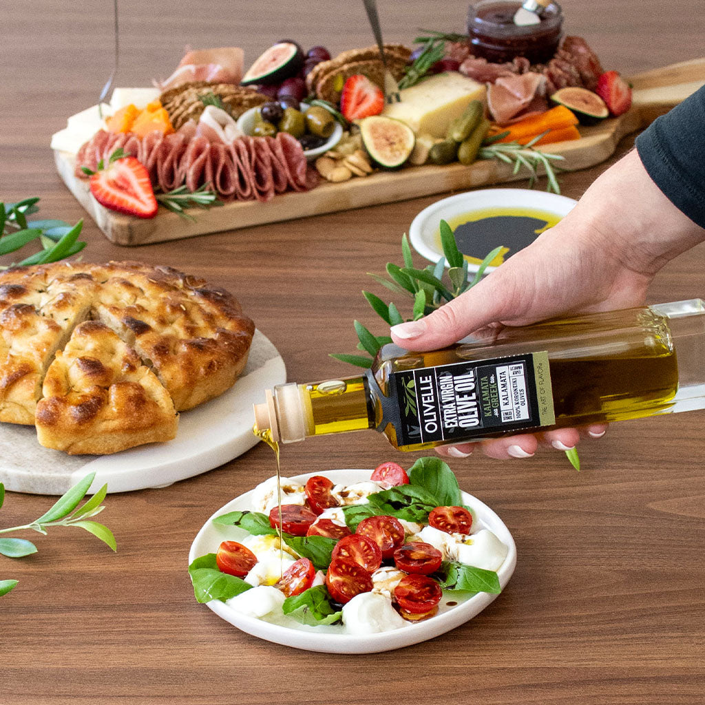 Person drizzling olive oil over a salad with a charcuterie board in the background