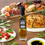 Bottle of olive oil on a wooden table with appetizers including bread, salad, and cured meats.