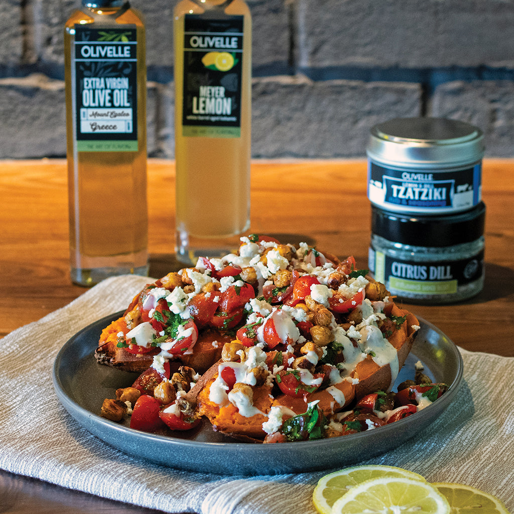 Plated dish with garnishes on a wooden table with Olvelle olive oil and tzatziki containers.