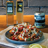 Plated dish with garnishes on a wooden table with Olvelle olive oil and tzatziki containers.