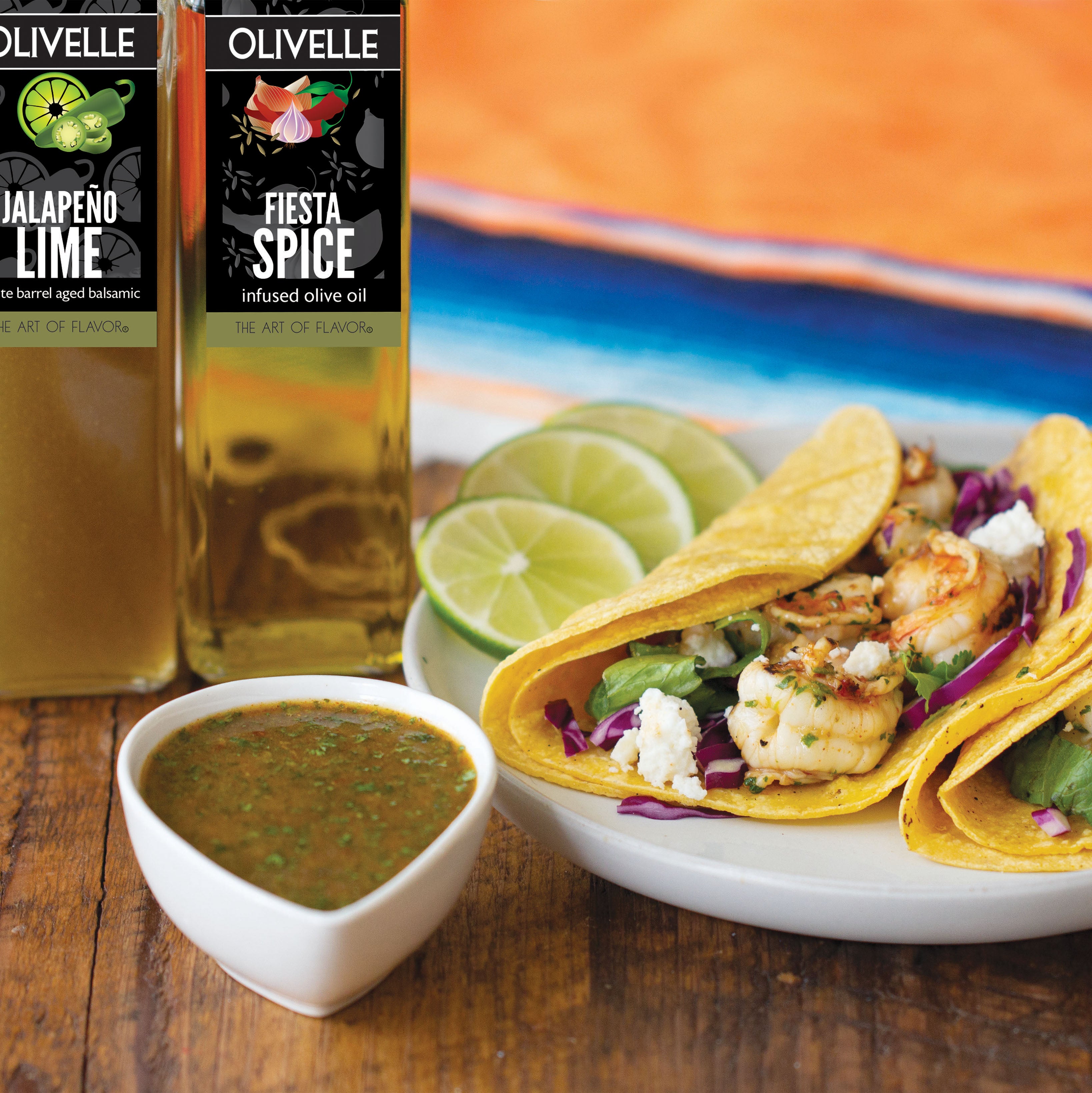 Olivelle jalapeno lime and fiesta spice olive oils with tacos and salsa on a wooden table.