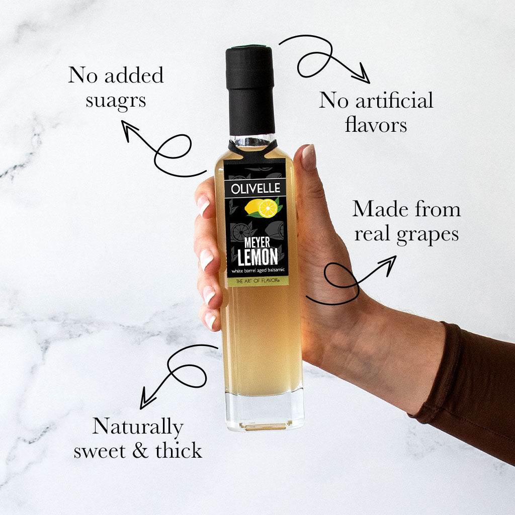 Bottle of Olivelle Meyer Lemon oil held by a hand on a marble background with text highlighting features.