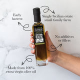Bottle of Olivelle olive oil held by a hand with text highlighting features on a marble background