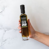 Hand holding a bottle of Olivelle olive oil against a white marble background