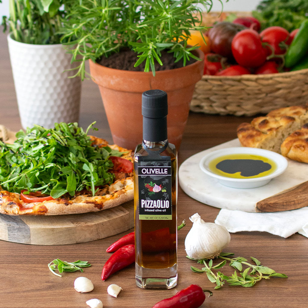 Olive oil bottle labeled 'Pizzaiolo' on a table with pizza, vegetables, and bread.