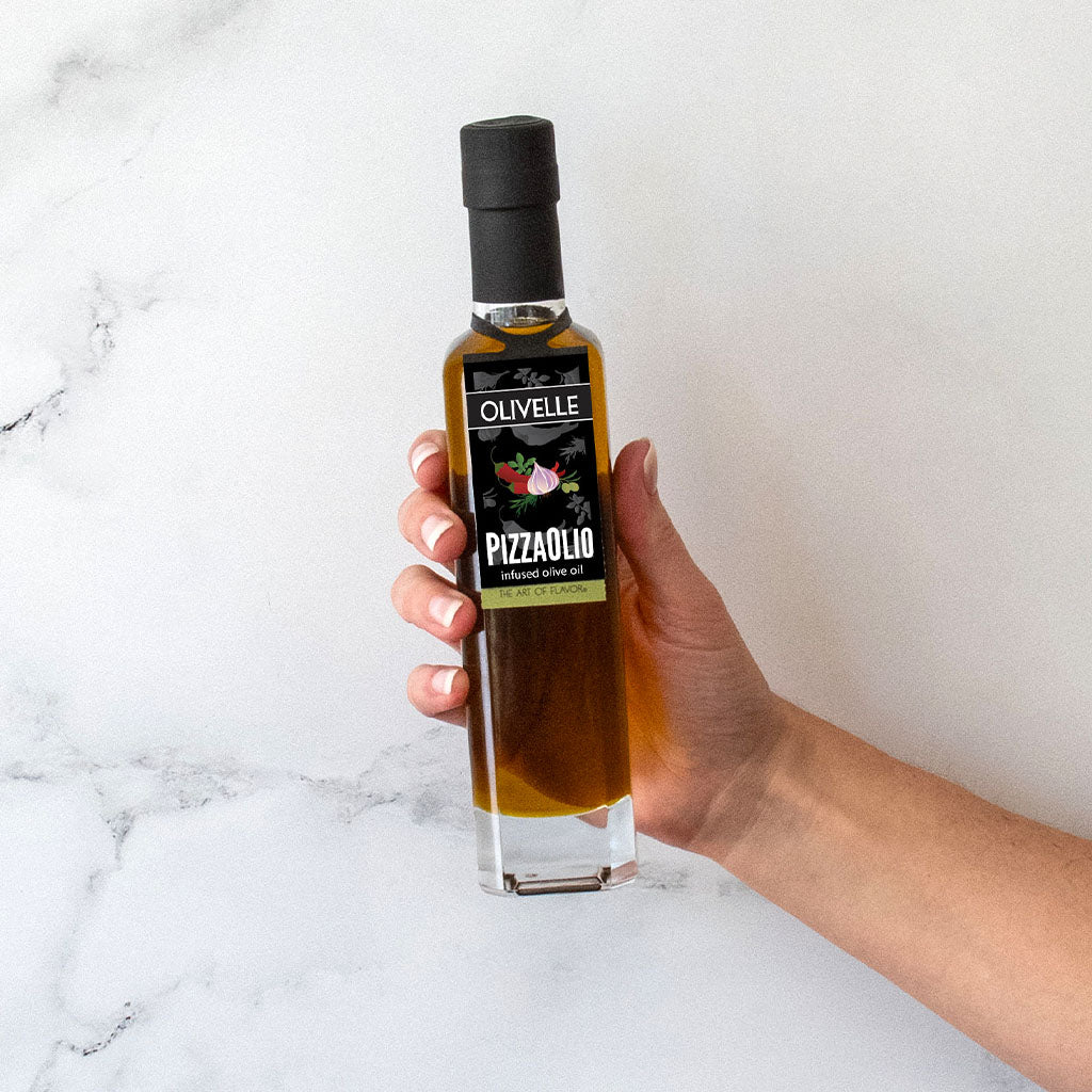 Hand holding a bottle of Olivelle Pizzolio olive oil against a white marble background
