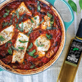 Dish with tomato sauce and cheese, basil leaves, and a bottle of Olivelle Basil Genovese olive oil.