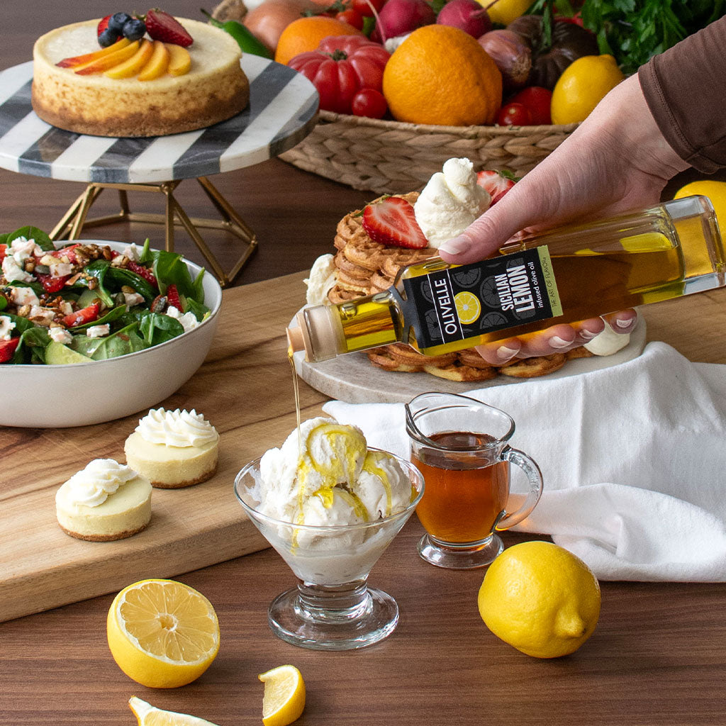 Table setting with various dishes including a dessert, salad, and pancakes being drizzled with olive oil.
