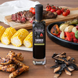 Olivelle Smoked balsamic vinegar bottle on a wooden table with grilled food and vegetables.