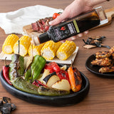 Person pouring olive oil over roasted vegetables on a wooden table with a bottle of olive oil.