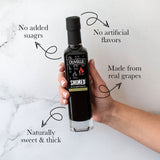Hand holding a bottle of Olivelle smoked balsamic vinegar with text highlighting its features on a marble background.