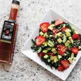 Salad with strawberries and avocados on a white plate next to a bottle of Olivelle strawberry dressing.