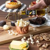 Butter being drizzled over popcorn with a variety of snacks on a wooden board.