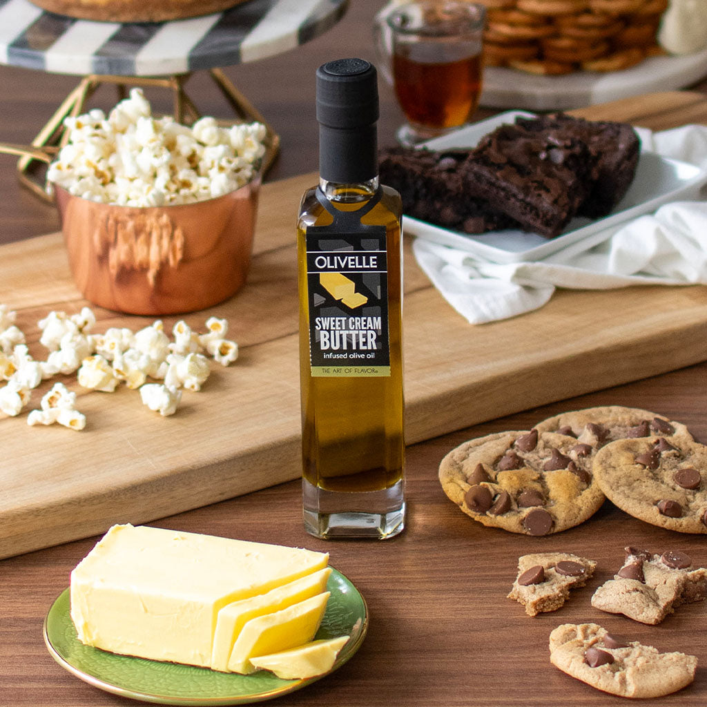 Bottle of Olivelle Sweet Cream Butter on a wooden table with popcorn, cookies, and brownies.