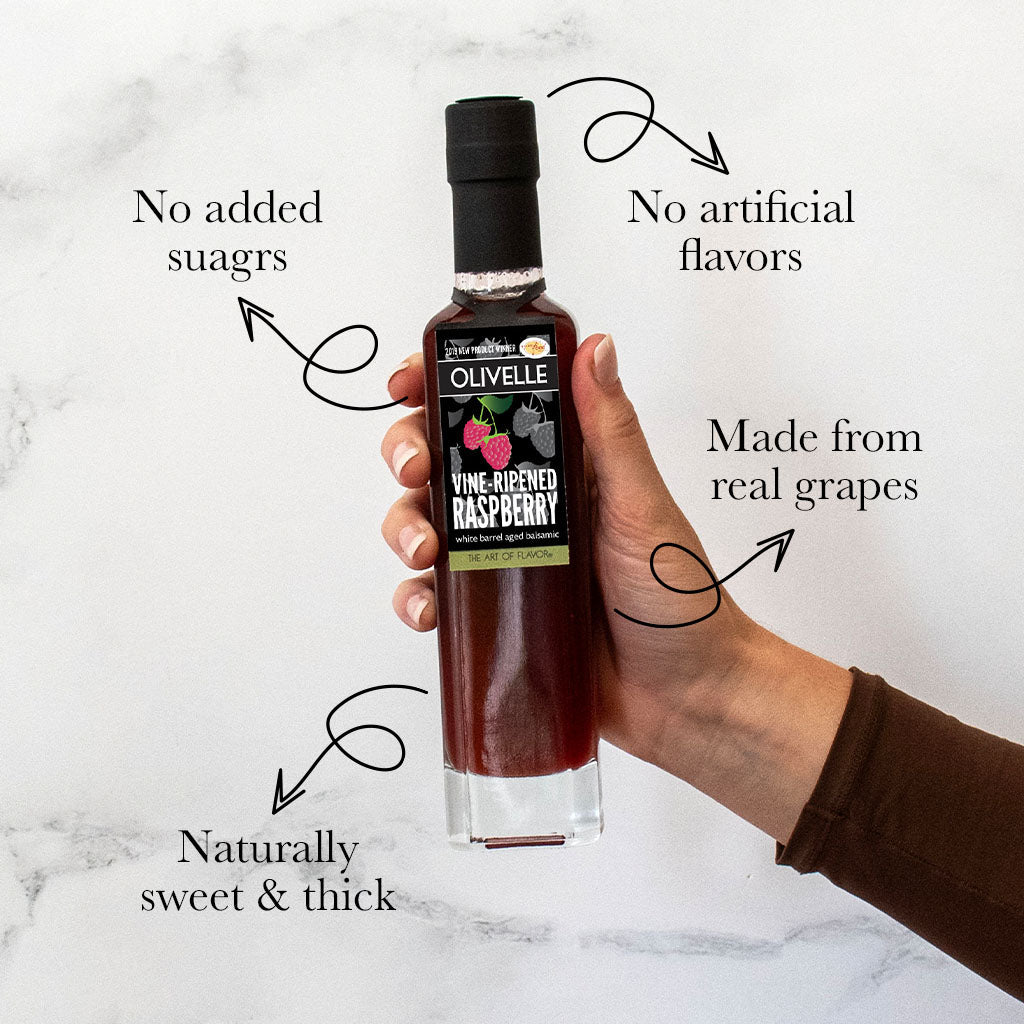 Hand holding a bottle of Olivelle raspberry product with text highlighting its features on a marble background