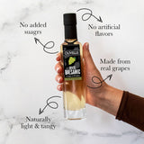 Hand holding a bottle of Olivelle White Balsamic vinegar with text highlighting its qualities on a marble background.