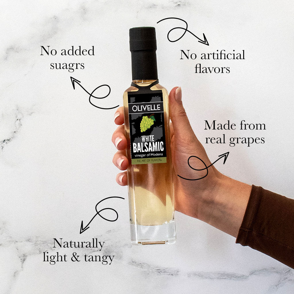 Hand holding a bottle of Olivelle White Balsamic vinegar with text highlighting its qualities on a marble background.