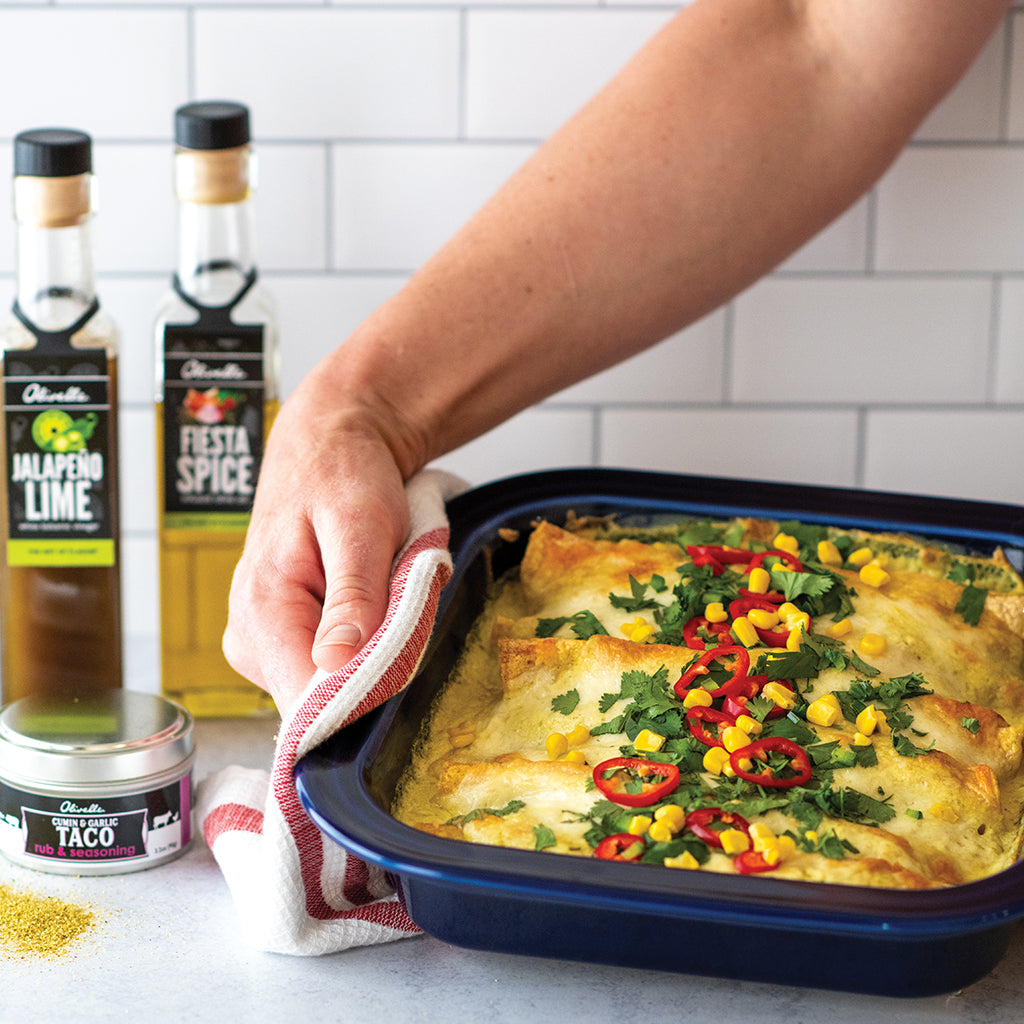 Person holding a tray of enchiladas with ingredients in the background