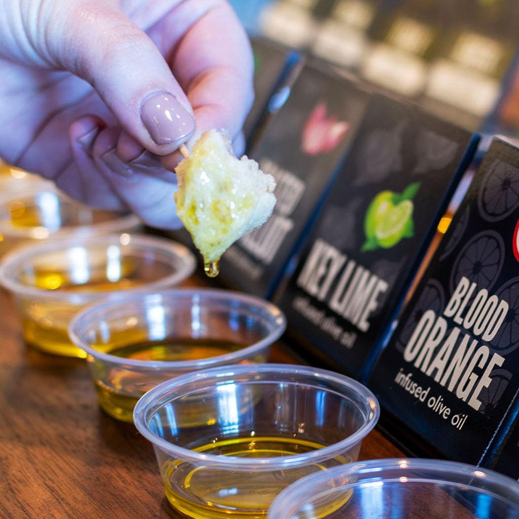 Person tasting key lime and blood orange infused olive oil with a focus on the oils in small containers.