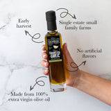 Bottle of Olivelle Garlic & Herb olive oil held by a hand with text highlighting features on a marble background.