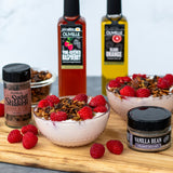 Two bowls of dessert with raspberries, Olvelle products, and vanilla bean on a wooden board.