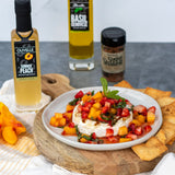 Plated appetizer with bocconcini, fruit salsa, and chips on a wooden board with Olivelle Summer Peach Liqueur and basil vinegar in the background.