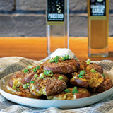 Smashed potatoes on plate with green onions with olive oil and prosecco in the background. 