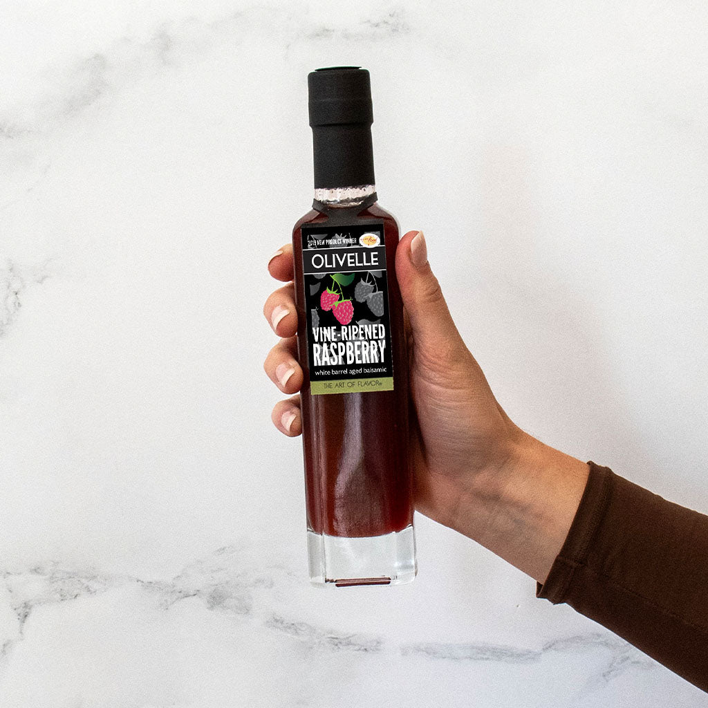 Hand holding a bottle of Olivelle raspberry vinegar on a marble surface
