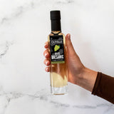 Hand holding a bottle of Olivelle White Balsamic vinegar on a marble surface