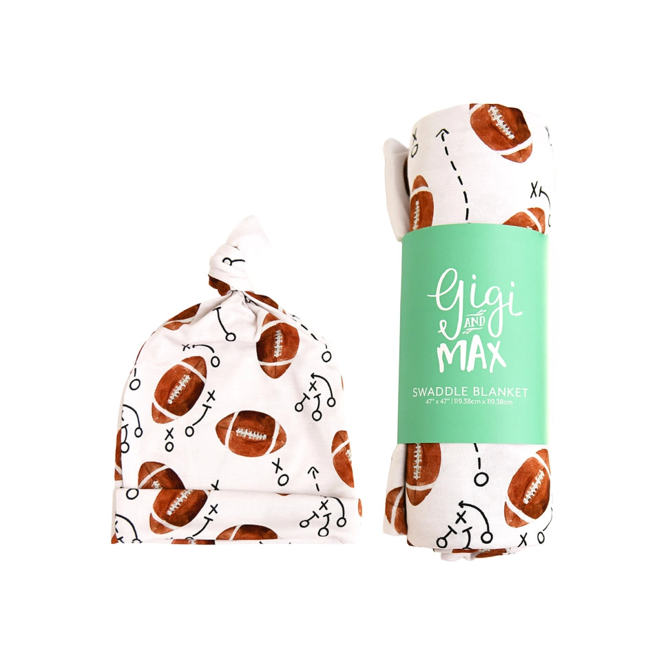 A football-themed swaddle blanket shown in two forms: one flat and tied, displaying the white fabric with brown footballs and black tactical play icons, and one rolled with a mint green paper band that reads 'Gigi and Max SWADDLE BLANKET'.