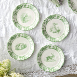 Set of four green-decorated plates with animal illustrations on a white lace tablecloth.