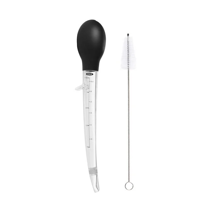 An angled baster with a black bulb and clear measurement markings, accompanied by a metal cleaning brush.