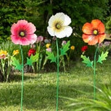 A metal garden stake featuring a poppy flower design in pink, white, and orange colors with a green stem, placed against a blurred garden background.
