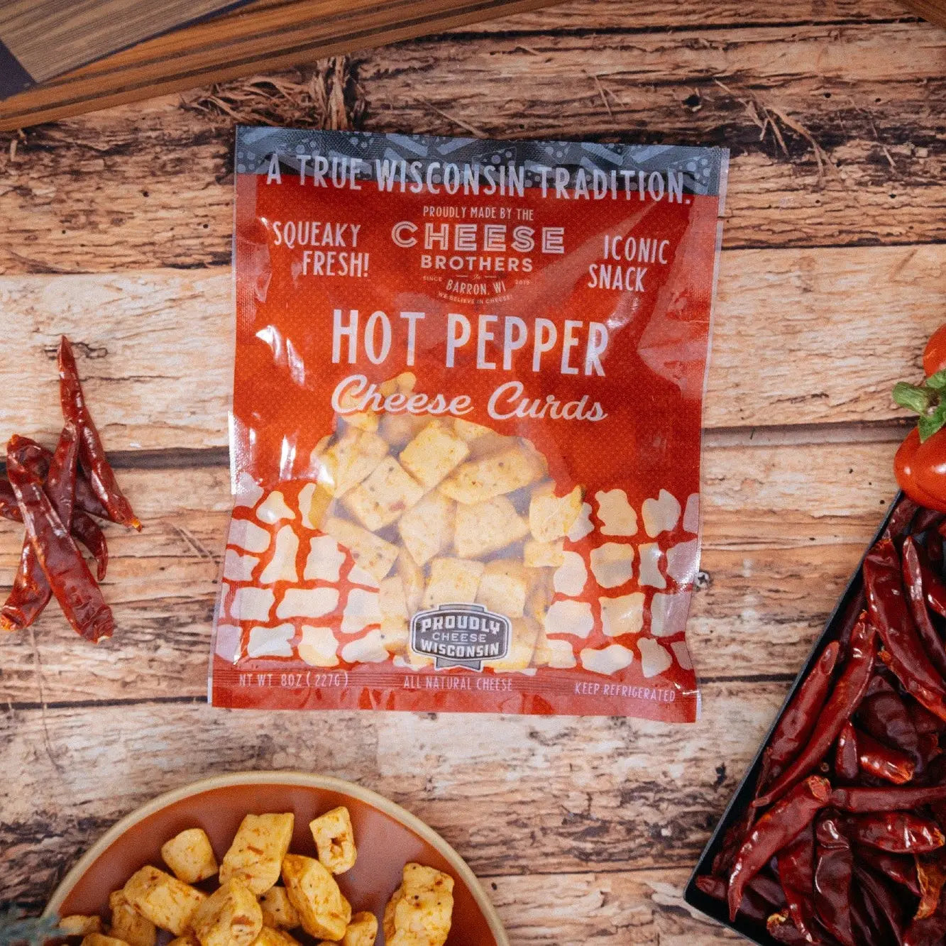 Packaged Hot Pepper Cheese Curds from Cheese Brothers on a wooden surface with cheese curds and hot peppers.
