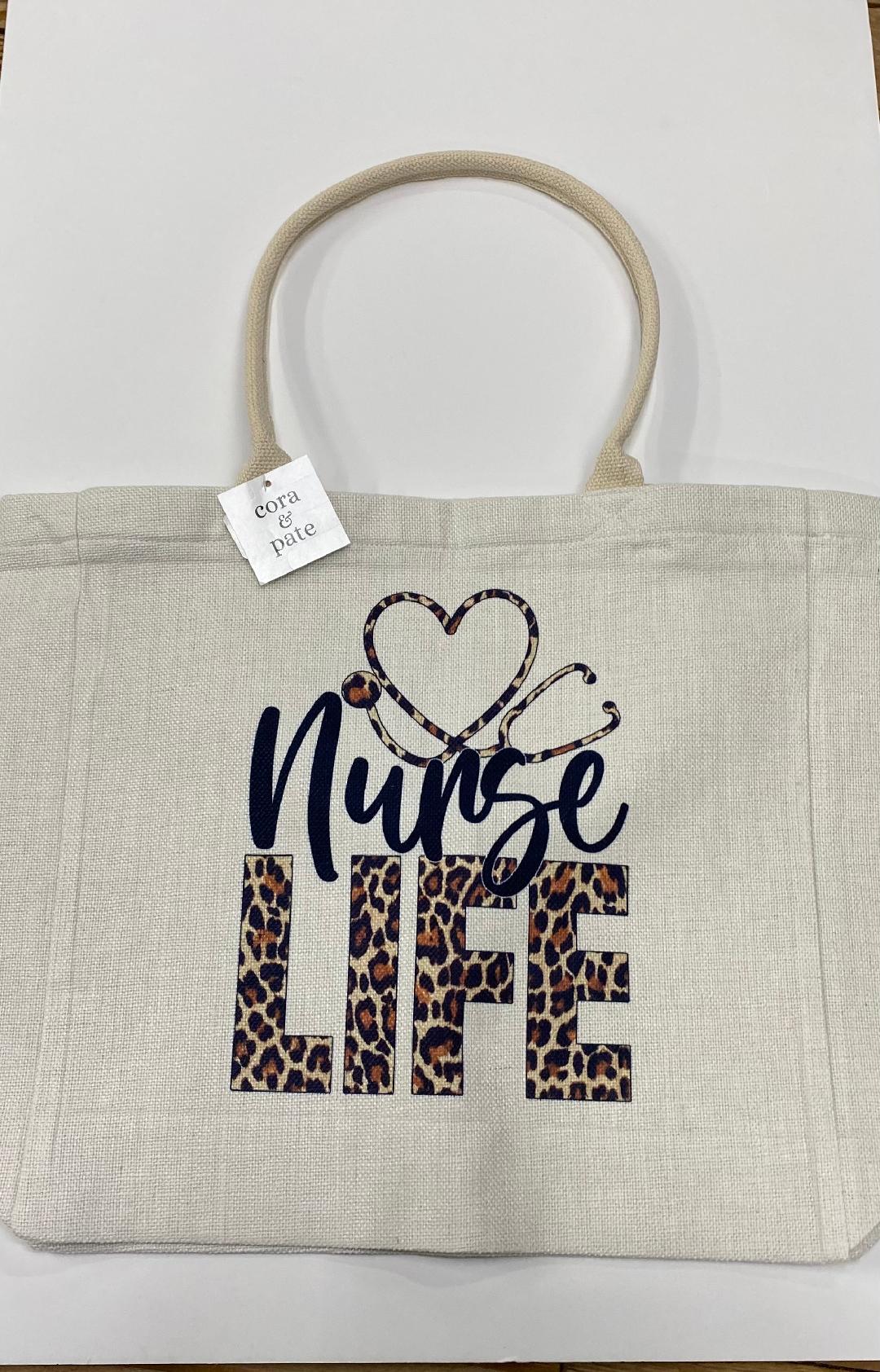 A beige canvas tote bag with 'Nurse Life' printed in blue and leopard patterned text, along with a heart shape.
