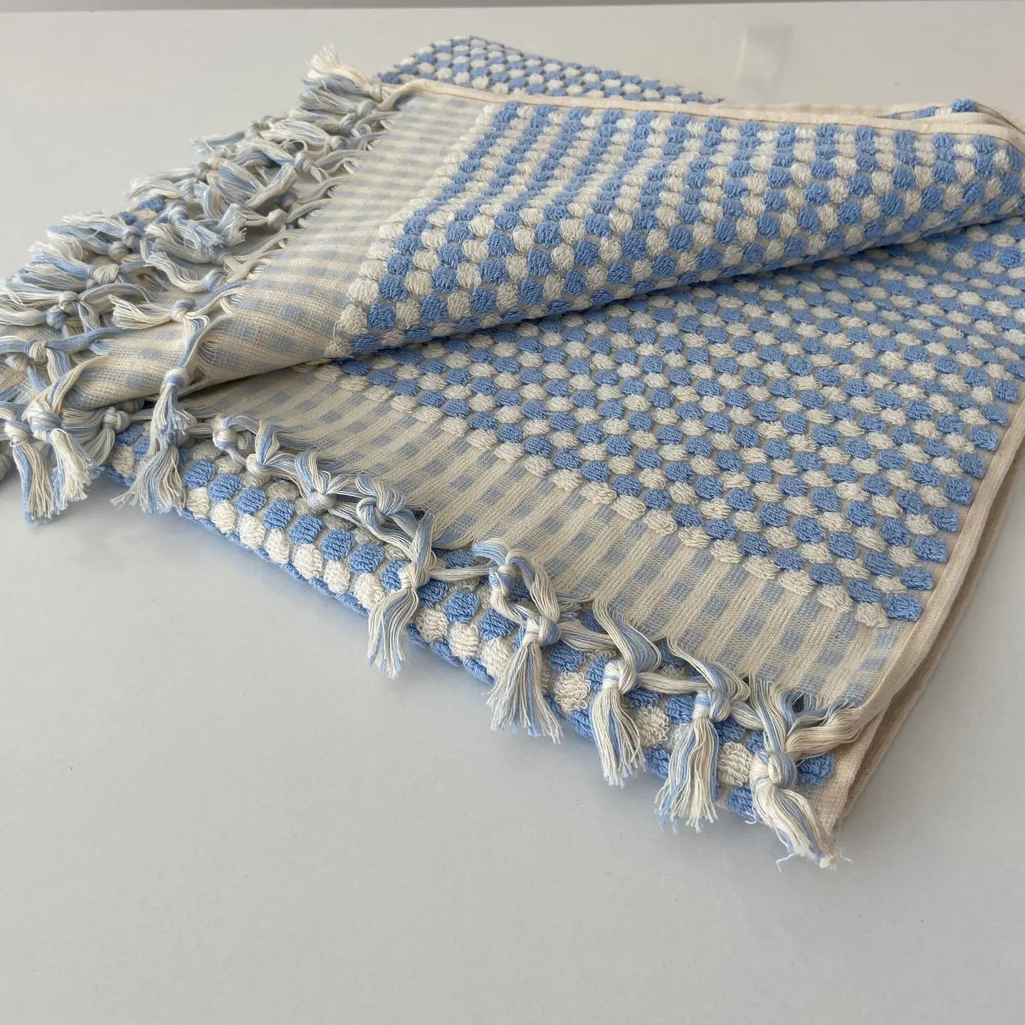 Blue and white checkered towel with tassels on a light gray background