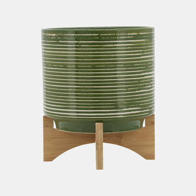 A green ceramic planter on a stand, with a cylindrical shape and a wooden base.