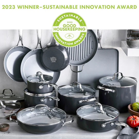 A set of black cookware including frying pans, saucepans, and a stockpot, all with glass lids and handles, displayed on a kitchen counter.