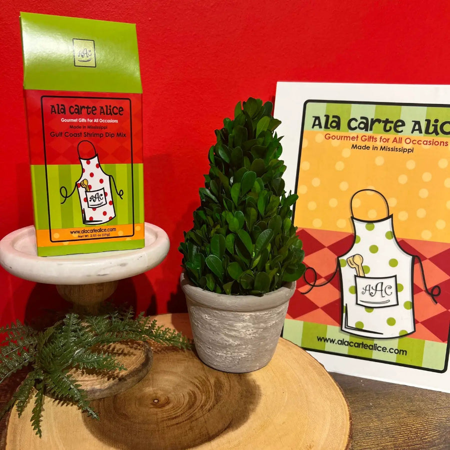 Potted plant on a wooden surface with 'Ala Carte Alice' packaging and promotional material in the background.