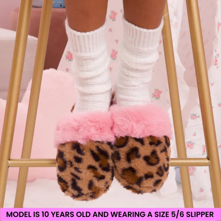Leopard print slippers with pink fur trim worn by a child on a gold stool.