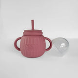 Pink textured sippy cup with straw and lid on a white background