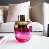 Pink and gold glass vase on a table with a blurred sofa in the background