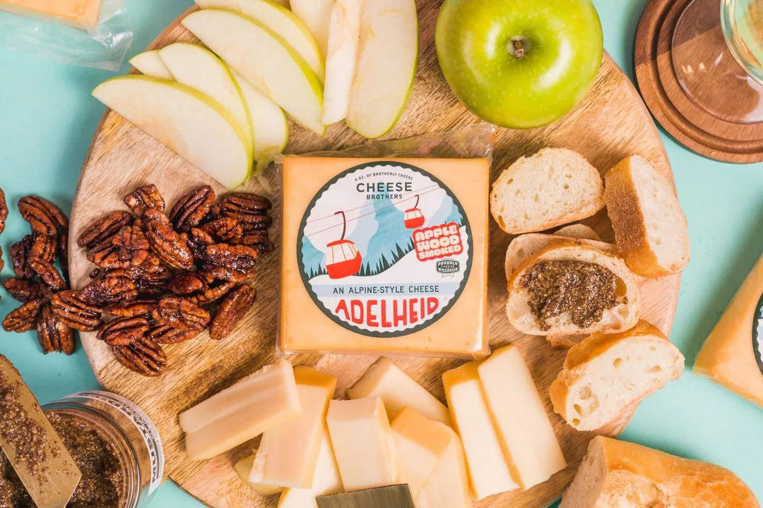 Cheese platter with Adelheids cheese, bread, apples, and nuts on a wooden board.