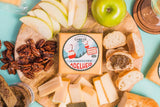 Cheese platter with Adelheids cheese, bread, apples, and nuts on a wooden board.