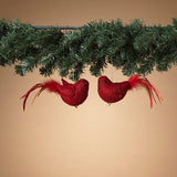 Two red cardinal bird ornaments with feather details, hanging from greenery against a beige background.
