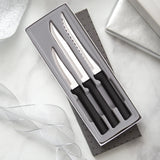 A three-piece kitchen knife set with black handles and silver stainless steel blades, presented in an open gray gift box on a white marble surface with decorative ribbon and a silver box in the background.