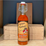 A bottle of Captain Rodney's Spicy Peach Barbecue Sauce with a label featuring an illustration of a pirate and peach slices, placed on a wooden surface.